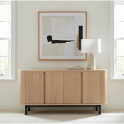Wooden sideboard in a room with abstract art and a lamp.
