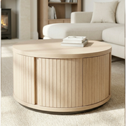 Round wooden coffee table in a living room setting with books on top